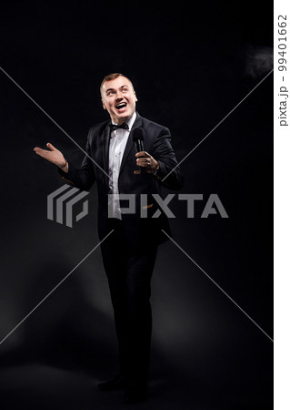 Full length of young man in costume with microphone on black background, singer, actor, leading Full length of young man in costume with microphone on black background, singer, actor, leading 99401662