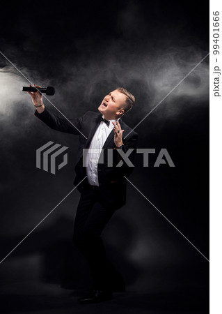 Full length of man in costume singing in microphone on black background, singer, actor, leader Full length of man in costume singing in microphone on black background, singer, actor, leader 99401666
