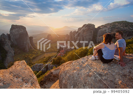 Love couple sitting on a rock overlooking Meteora at sunset. Travel in Greece. Love couple sitting on a rock overlooking Meteora at sunset. Travel in Greece. 99405092