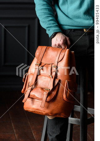 Orange leather oldfashioned backpack in a mans hands Orange leather oldfashioned backpack in a mans hands 99405433
