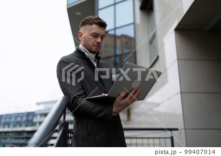 young businessman in a coat working on a laptop near the office center 99407014
