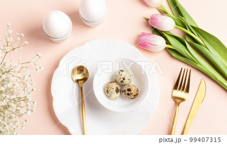 Festive Easter table decoration idea with eggs, spring flowers, golden cutlery, beautiful plates. Holiday image in gentle peach color. Top view, flat lay. Festive Easter table decoration idea with eggs, spring flowers, golden cutlery, beautiful plates. Holiday image in gentle peach color. Top view, flat lay. 99407315