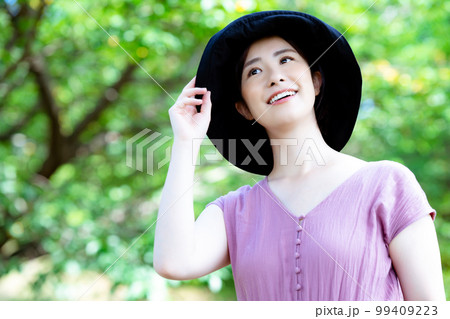 新緑の公園でリフレッシュする帽子をかぶったワンピースの女性 99409223