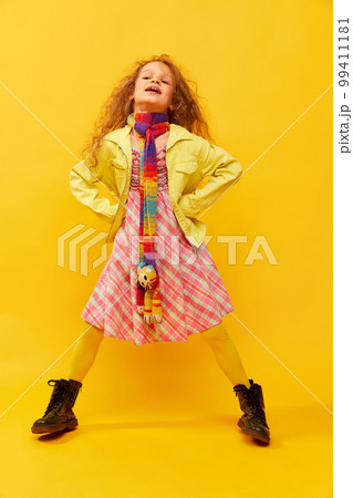 Extraordinary look. Little cute girl, child with curly hair posing in bright clothes over yellow studio background. Concept of childhood, emotions, fun Extraordinary look. Little cute girl, child with curly hair posing in bright clothes over yellow studio background. Concept of childhood, emotions, fun 99411181