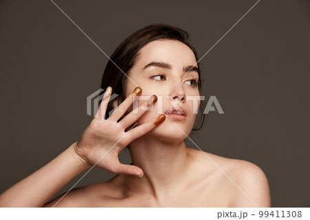 Sparkling nude eyeshadow swatches on fingers. Portrait of young beautiful girl with brown hair posing over dark grey studio background. Concept of natural beauty, skin care, cosmetology 99411308