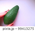 Avocado on a white background. Female hand with red manicure holds a whole avocado. Stock photography for advertising natural products, texts about the right choice of vegetables, fruits. Copy space 99413275