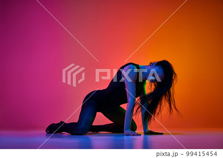 Dynamic studio shot of talented female dancer performing on stage over gradient pink orange background in neon light Dynamic studio shot of talented female dancer performing on stage over gradient pink orange background in neon light 99415454