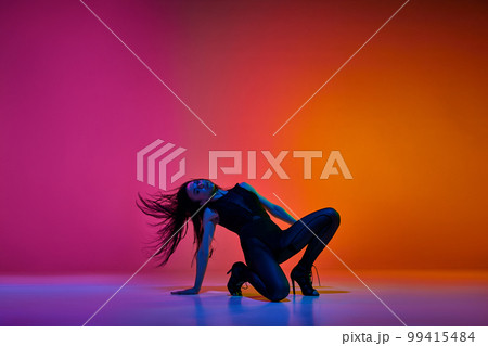 Passion in movements. Young woman performing high heel stiletto dance over gradient pink red studio background in neon light Passion in movements. Young woman performing high heel stiletto dance over gradient pink red studio background in neon light 99415484