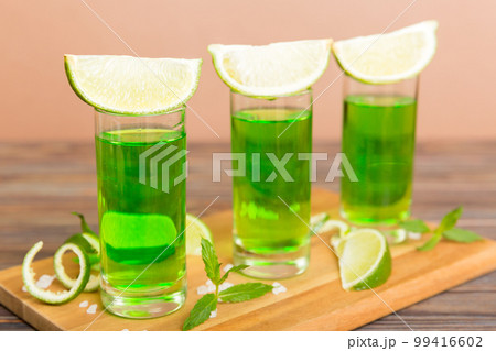 Sweet refreshing mint liqueur, with ice and mint leaves on table background, Shots with lime slice and mint flat lay 99416602