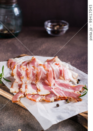 Raw smoked bacon and rosemary on a cutting board on the table. Hearty snack. Vertical view 99417045