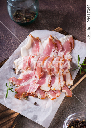 Raw bacon slices on paper on a cutting board on the table. Hearty snack. Vertical view 99417046