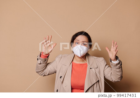 Shocked middle-aged multi-ethnic woman in medical mask, gesturing, expressing stupefaction looking at camera, isolated beige background. Quarantine, self isolation, social distance concept. Copy space Shocked middle-aged multi-ethnic woman in medical mask, gesturing, expressing stupefaction looking at camera, isolated beige background. Quarantine, self isolation, social distance concept. Copy space 99417431