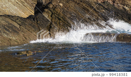 Small ocean waves reaching the rocks, in winter sunshine, in Cornwall, UK 99418381