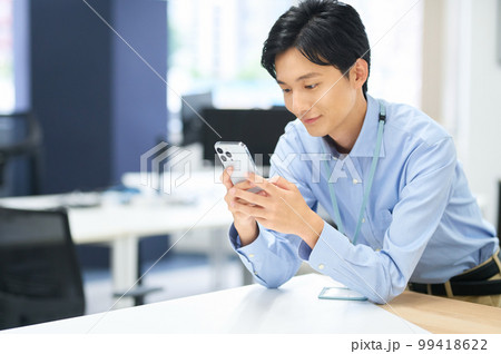 オフィスで働くスマホを持った私服の若い男性ビジネスマン 99418622