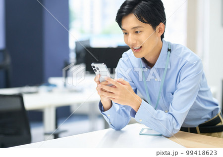 オフィスで働くスマホを持った私服の若い男性ビジネスマン 99418623