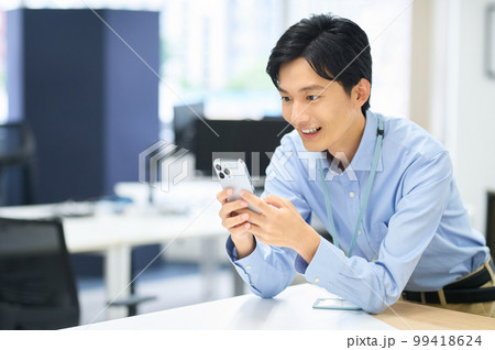 オフィスで働くスマホを持った私服の若い男性ビジネスマン 99418624
