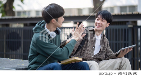 Two young Asian male college students discussing and working on their school project together Two young Asian male college students discussing and working on their school project together 99418690