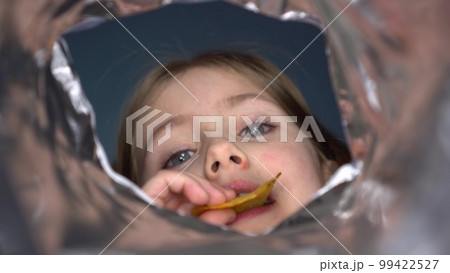 The girl looks into a pack of snacks and eats. The child eats chips from a pack. First-person view from a bag of chips. The girl looks into a pack of snacks and eats. The child eats chips from a pack. First-person view from a bag of chips. 99422527