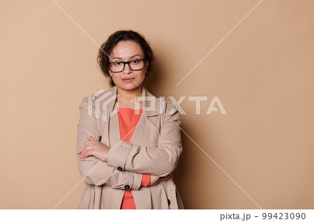 Confident portrait of a multi-ethnic beautiful middle-aged woman, wearing stylish eyeglasses, confidently looking at camera, isolated on beige color background. Copy advertising space. 99423090