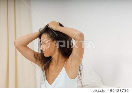 Female girl with hangover headache, time to get up for work. Beautiful young woman, dressed in silk negligee of delicate blue color, is sitting in cozy bed in the bedroom, holding her head. 99423756