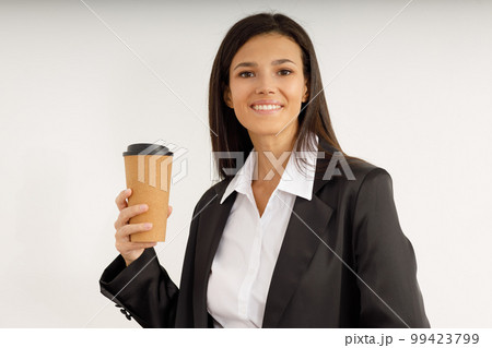 Portrait of happy pretty young woman in business suit holding paper cup of coffee in her hands on isolated white background. Studio shot of attractive brunette girl with snow-white smile. Portrait of happy pretty young woman in business suit holding paper cup of coffee in her hands on isolated white background. Studio shot of attractive brunette girl with snow-white smile. 99423799