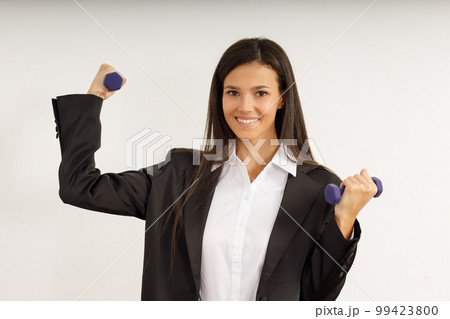 Attractive girl with dark hair in stylish business suit and white shirt holds small female dumbbells. Portrait of happy smiling young woman with sports equipment on isolated white background. Attractive girl with dark hair in stylish business suit and white shirt holds small female dumbbells. Portrait of happy smiling young woman with sports equipment on isolated white background. 99423800
