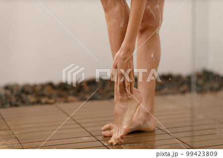 Woman under the trickles of water in pleasure shower. Girl under the spray of water. Wet legs close up 99423809