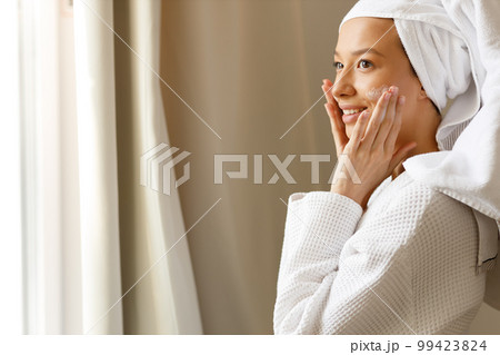 Young woman in white robe and with towel on her head pours applying lotion, gel or hand moisturizer from white bottle into the palm of her hand. Healthy body care after shower. Attractive girl in the Young woman in white robe and with towel on her head pours applying lotion, gel or hand moisturizer from white bottle into the palm of her hand. Healthy body care after shower. Attractive girl in the 99423824