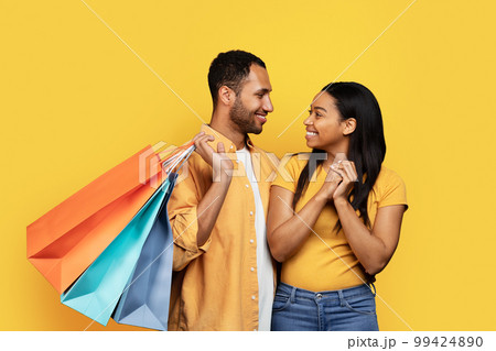 Smiling young african american boyfriend hugs woman, hold many packages with purchases, enjoy buy 99424890