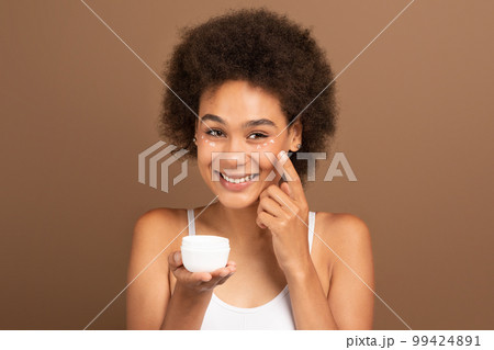 Beauty care and daily procedures. Smiling young black curly lady with perfect skin hold jar of moisturizing cream 99424891