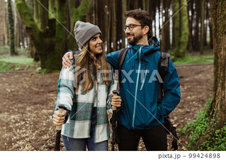 Smiling millennial caucasian male and woman in jackets, backpacks and trekking sticks travel 99424898