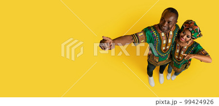 Loving black spouses pointing at copy space on yellow 99424926