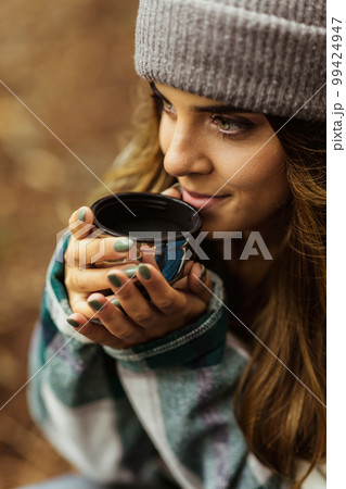 Smiling millennial caucasian woman in jacket and hat drink hot tea cup, travel in cold forest, enjoy adventure outdoor 99424947
