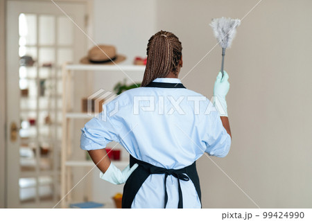 Back view of black woman holding cleaning brush, living room interior 99424990