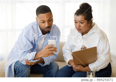Black man patient showing woman therapist content on smartphone Black man patient showing woman therapist content on smartphone 99425071