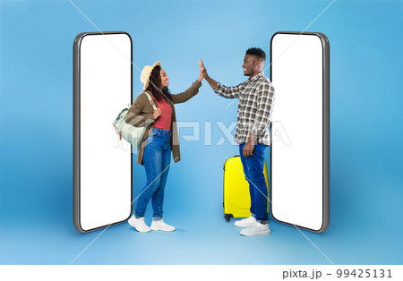 Black couple with luggage high fiving each other on blue 99425131