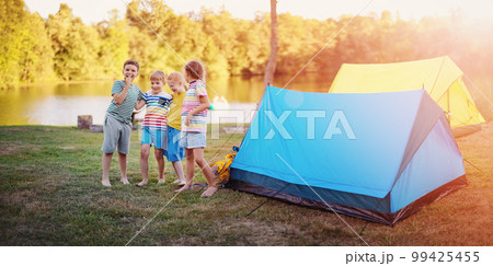 Group of four children standing near colourful tents in nature. Group of four children standing near colourful tents in nature. 99425455