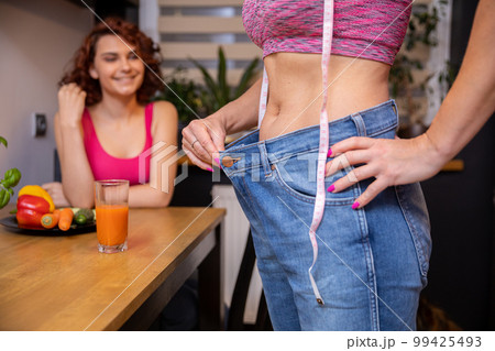 A woman shows off the effects of weight loss by stretching the waistband of loose pants. A woman shows off the effects of weight loss by stretching the waistband of loose pants. 99425493