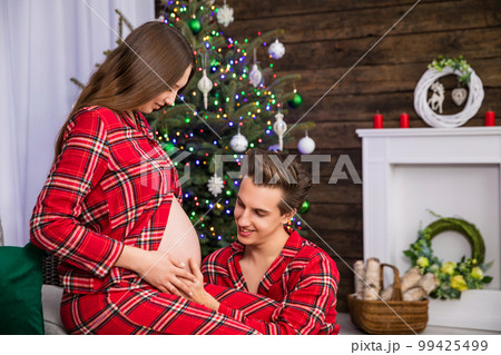 A pregnant woman sits on a couch while a man kneels in front of her. 99425499