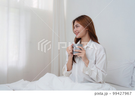 Beautiful asian woman has woken up on a white bed and holding coffee in the morning at home. lifestyle concept. Beautiful asian woman has woken up on a white bed and holding coffee in the morning at home. lifestyle concept. 99427967