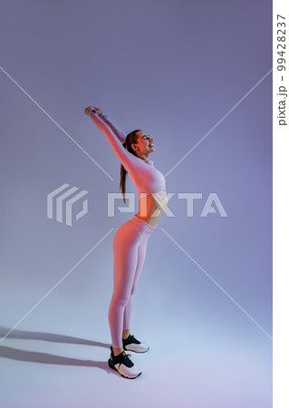 Athletic woman wearing sportswear doing warm-up before training session in gym on studio background Athletic woman wearing sportswear doing warm-up before training session in gym on studio background 99428237
