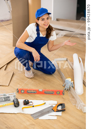 Female repairer installing laminate flooring, making presenting gesture Female repairer installing laminate flooring, making presenting gesture 99428870