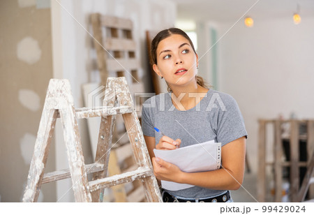 Woman with documents in her hands checks the quality of the completed repairs in cottage room 99429024