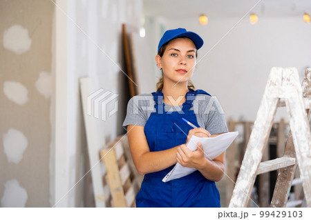 Woman in blue overalls checking completed construction work on drawing 99429103