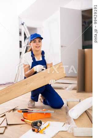 Woman construction worker setting wooden laminate board on floor 99429191