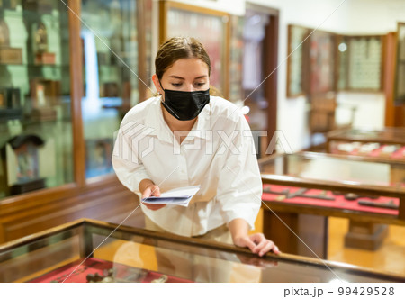 Woman exploring artworks in glass case in museum Woman exploring artworks in glass case in museum 99429528