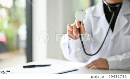Cropped image of an Asian female doctor in uniform holding a stethoscope at her desk 99431736