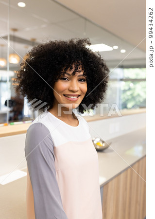 Vertical image of happy biracial businesswoman looking at camera in office 99434262