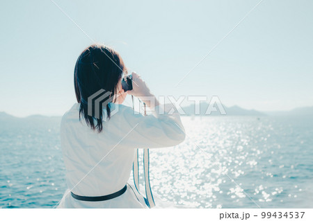 浜辺に佇むカメラを持った若い女性の写真 浜辺に佇むカメラを持った若い女性の写真 99434537