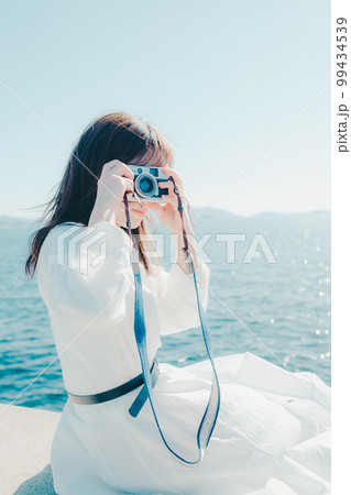 浜辺に佇むカメラを持った若い女性の写真 99434539